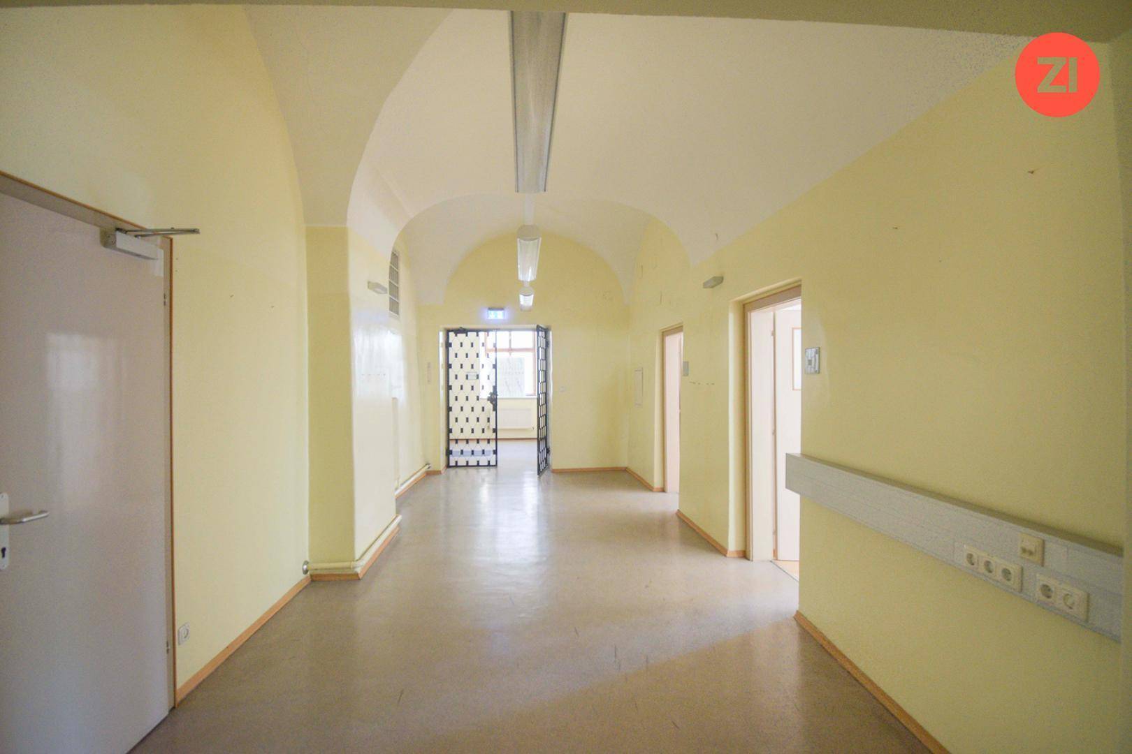 Langer Flur mit gelben Wänden, gewölbter Decke und mehreren Türen, gut beleuchtet und funktional.