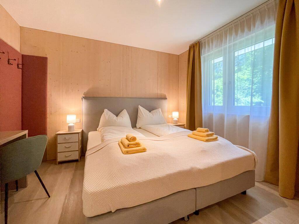 Helles Schlafzimmer mit Doppelbett, Nachttischen und Blick auf die grüne Umgebung.