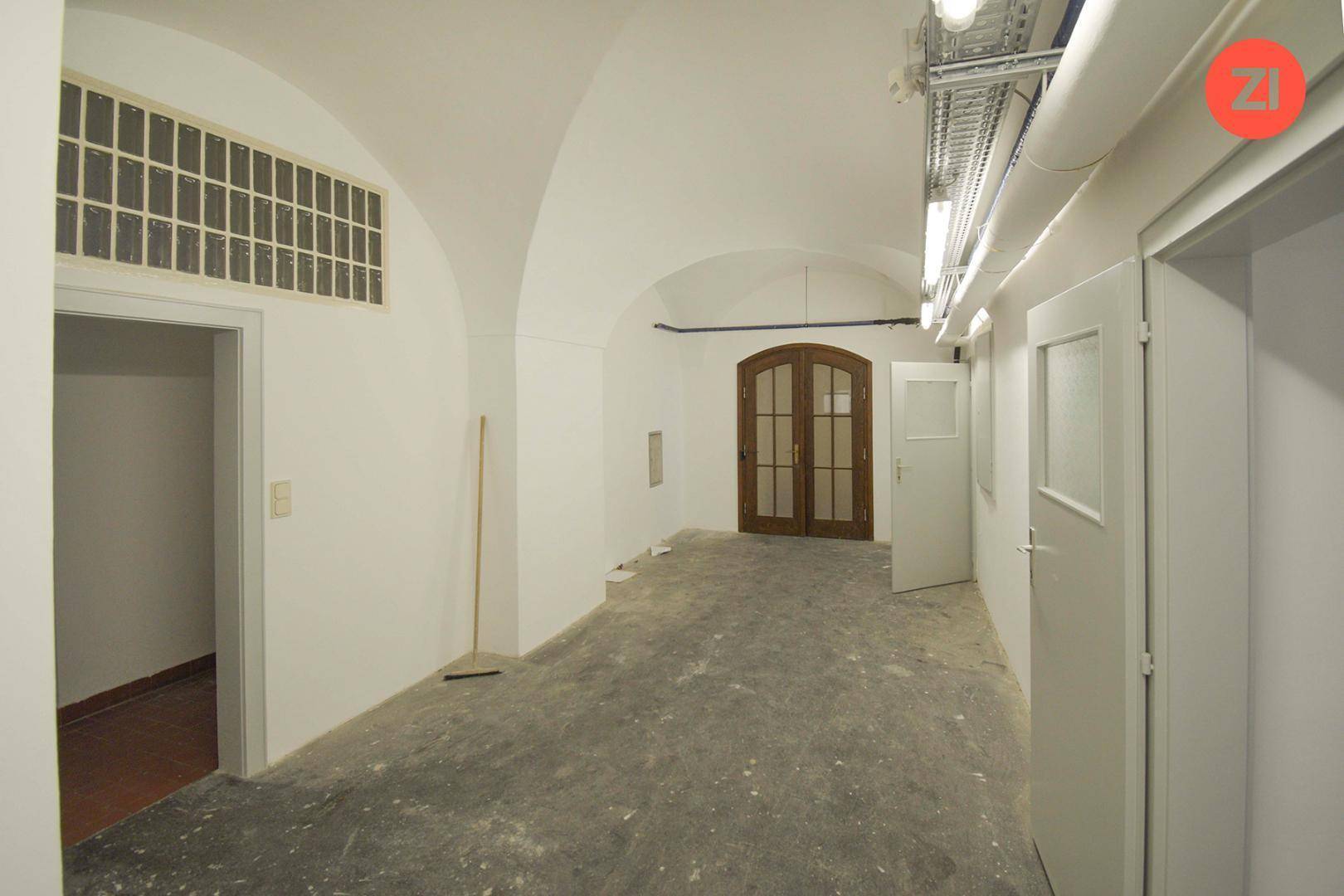 Langer Flur mit gewölbter Decke, Holztüren und sichtbaren Leitungen, gut beleuchtet und geräumig.