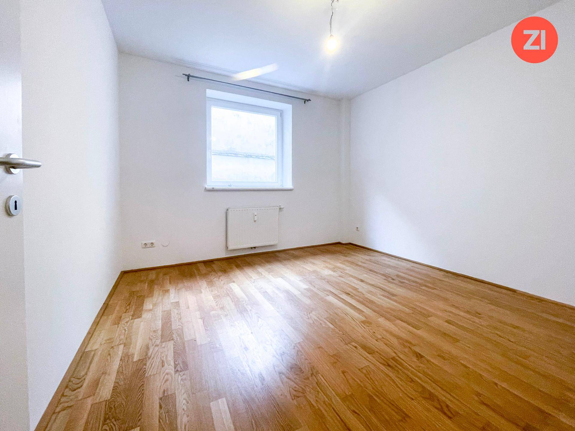 Geräumiges Zimmer mit hellem Parkettboden und einem Fenster, das viel Tageslicht hereinlässt.