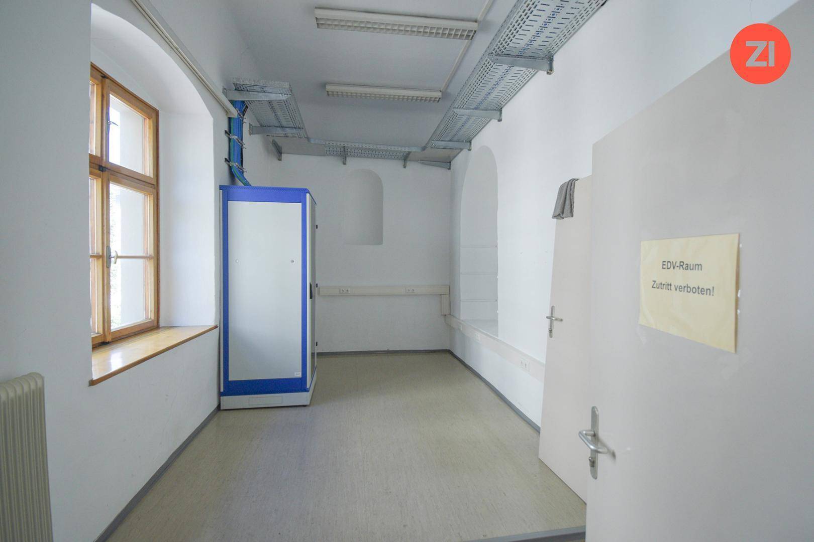 EDV-Raum mit Serverschrank, Kabeltrassen an der Decke und einem Fenster für Belüftung und Licht.