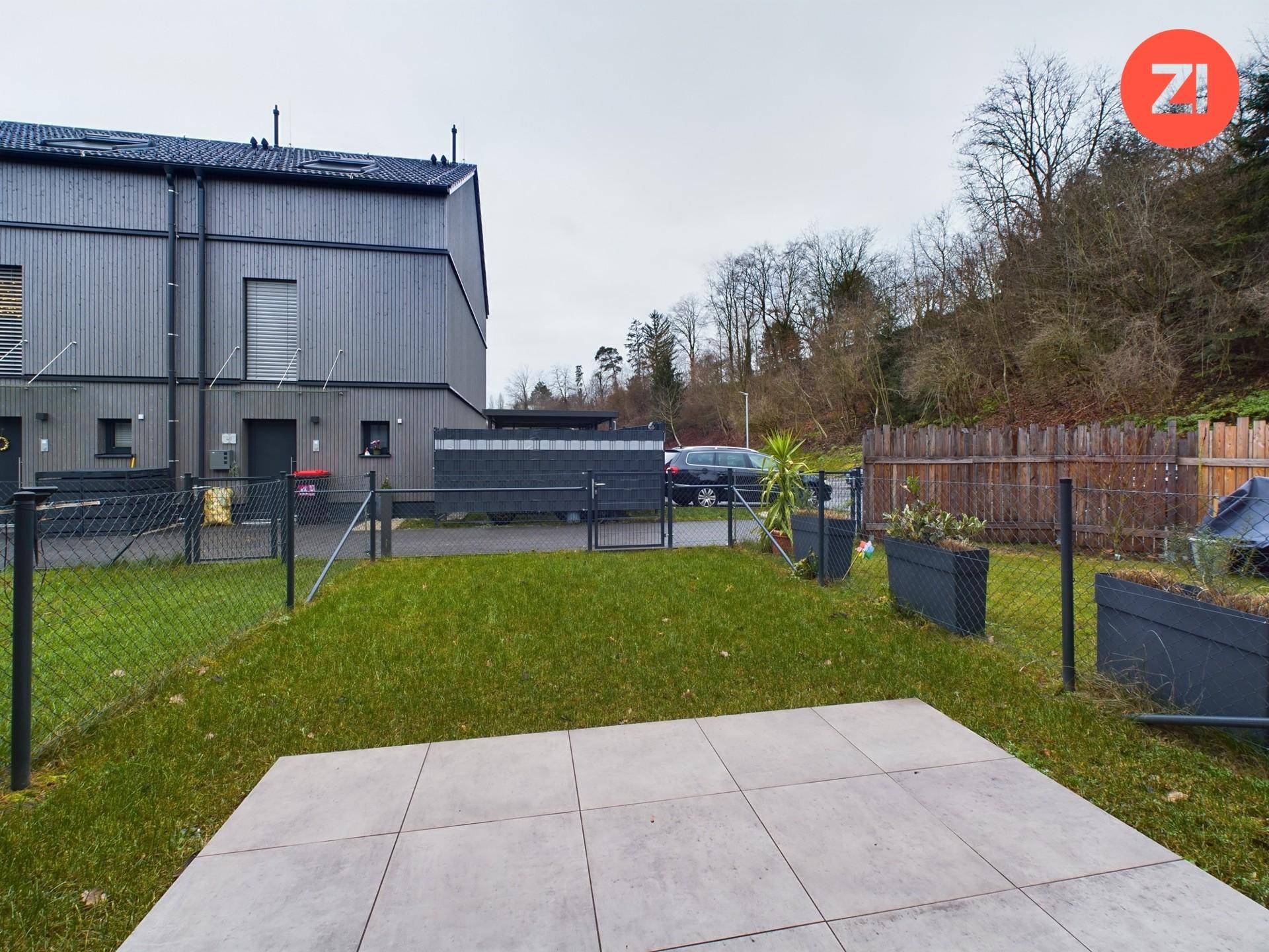 Kleiner privater Garten mit Rasenfläche und gepflasterter Terrasse hinter dem Haus.