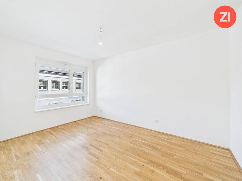 Helles Schlafzimmer mit Parkettboden und einem großen Fenster, das viel Tageslicht hereinlässt.