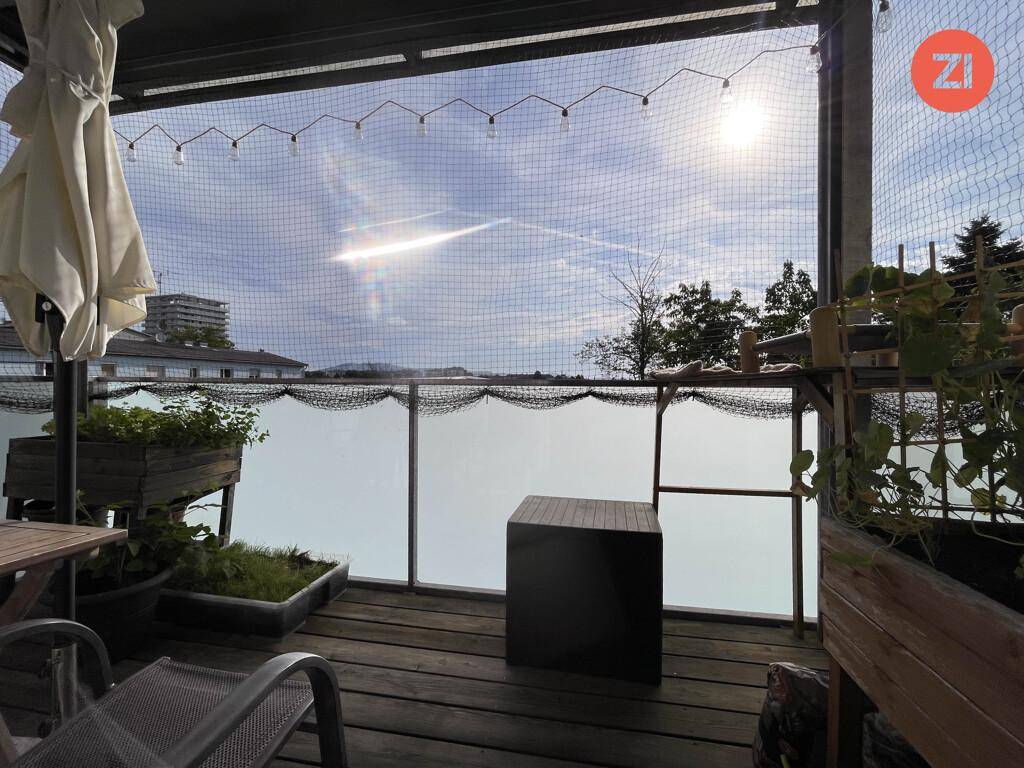 Sonniger Balkon mit Holzboden, Pflanzen und Blick ins Grüne.