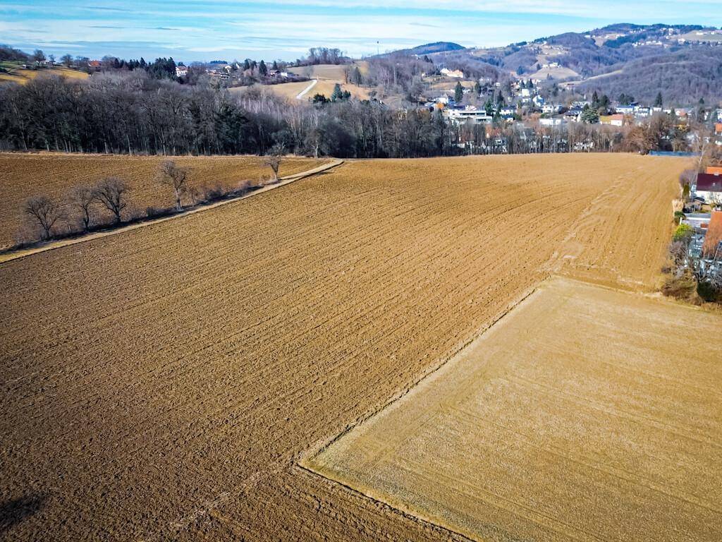 Weitläufige Ackerflächen mit angrenzenden Feldern und vereinzelten Häusern am Horizont.