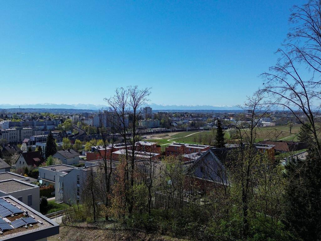Weitblick über eine Stadtlandschaft mit bewaldeten Hügeln und einer beeindruckenden Bergkulisse am Horizont.