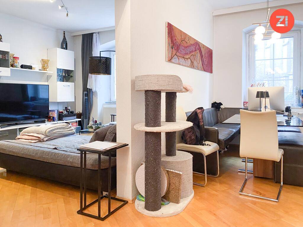 Geräumiger Wohnbereich mit Holzboden, Sofa und einem Katzenkratzbaum, hell und offen gestaltet.
