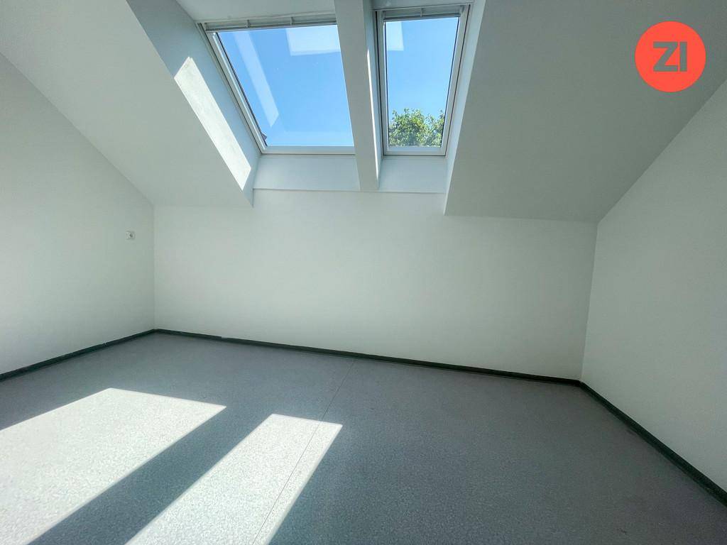 Geräumiges Zimmer im Dachgeschoss mit grauem Boden und hellen Dachfenstern für viel Tageslicht.