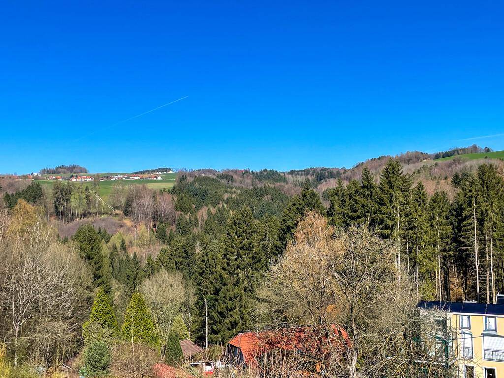 Panoramablick über bewaldete Hügel und ländliche Siedlungen unter blauem Himmel.