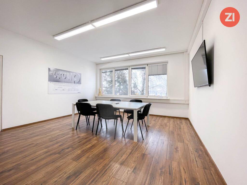Heller Konferenzraum mit großem Tisch, Laminatboden und Wandfernseher, geeignet für Besprechungen.