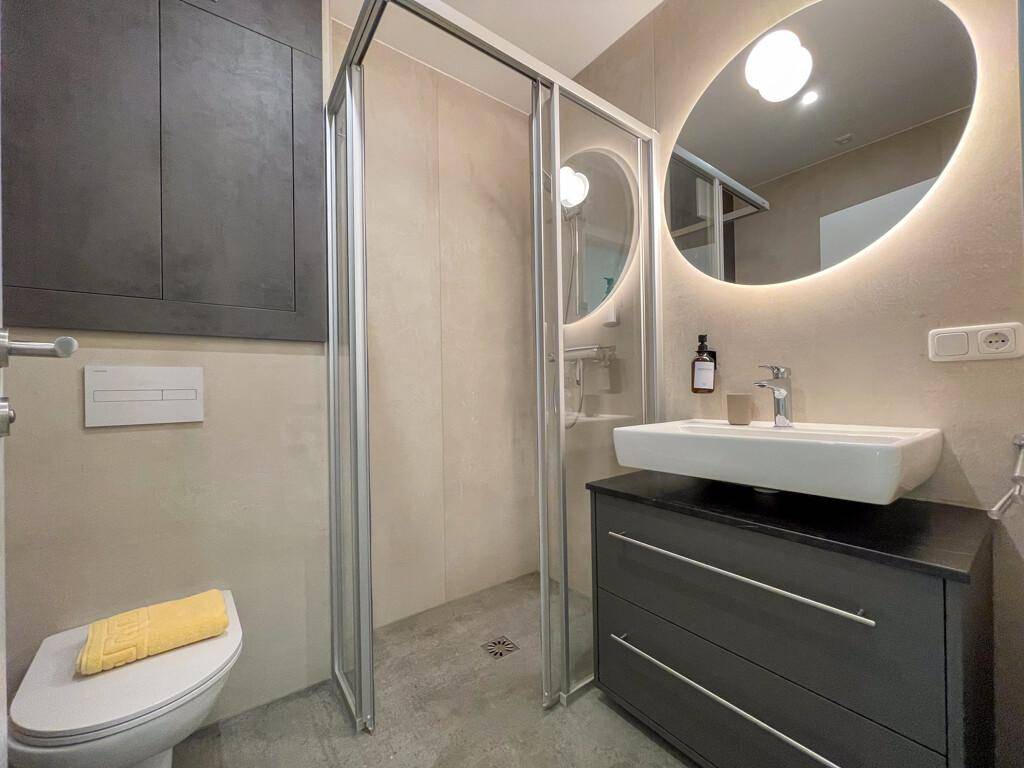 Modernes Badezimmer mit begehbarer Dusche, beleuchtetem Spiegel und stilvollem Waschtisch.