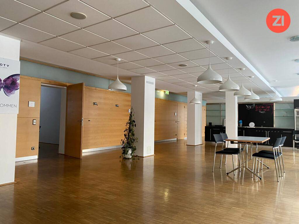 Großer Konferenzraum mit Holzboden, Säulen und moderner Beleuchtung, vielseitig nutzbar.