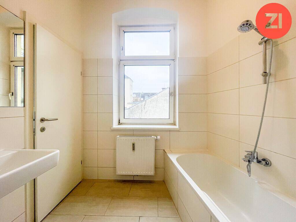 Badezimmer mit Badewanne, Waschbecken und Fenster für Tageslicht.