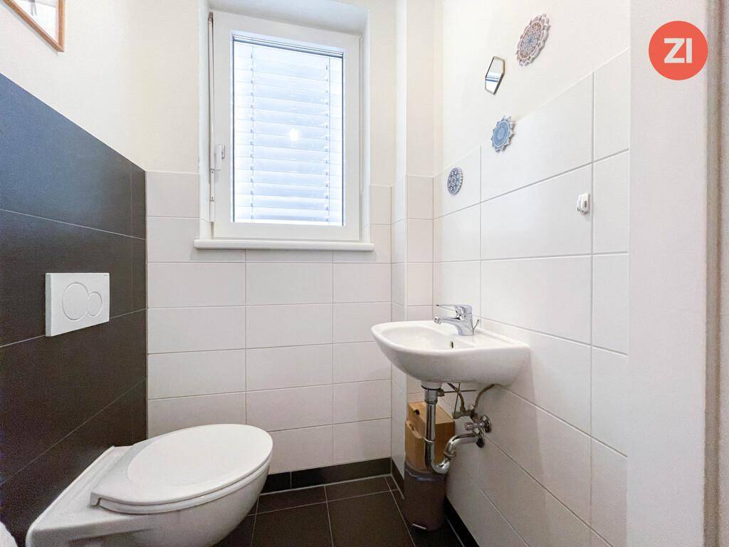 Separates WC mit Fenster, Waschbecken und weißen Wandfliesen.