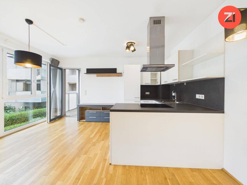 Offener Wohnbereich mit integrierter Küche, Parkettboden und direktem Zugang zum Balkon.