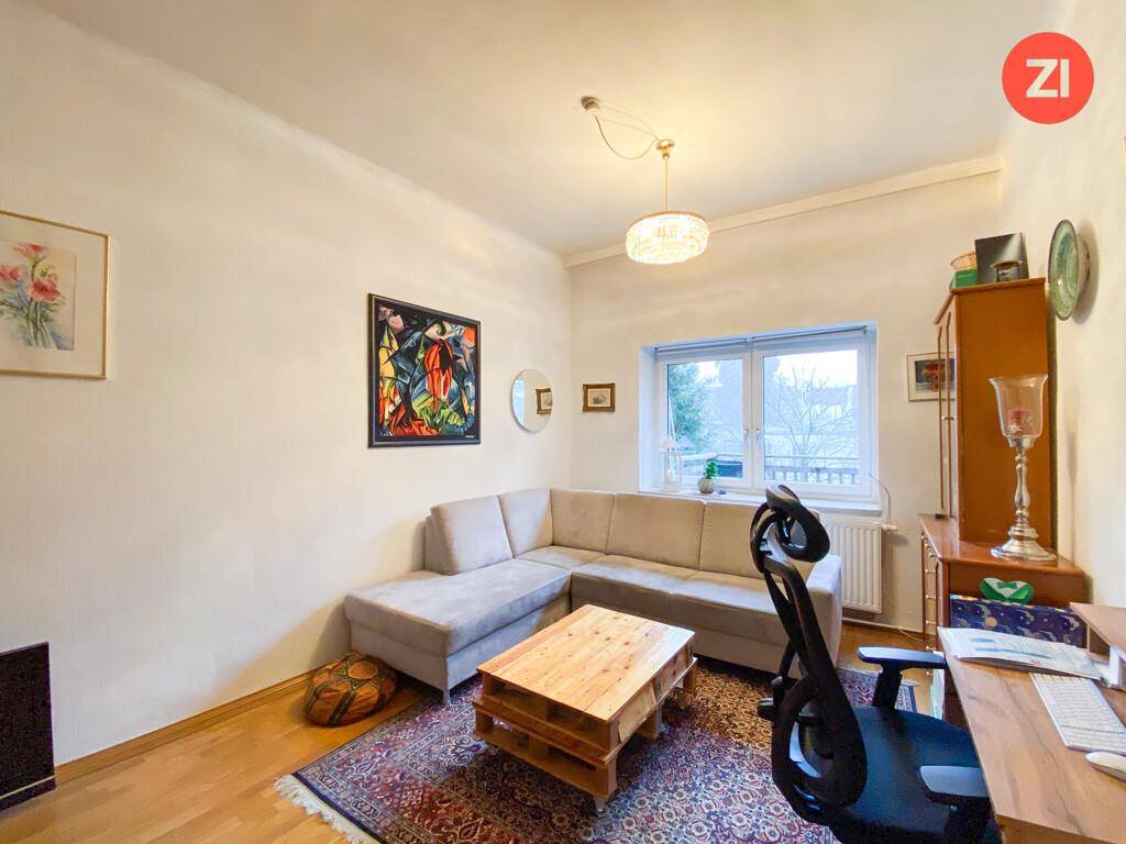 Wohnzimmer mit Ecksofa, Holztisch und einem Arbeitsbereich am Fenster, hell und funktional.