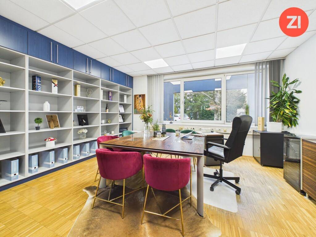 Modernes Büro mit großem Holztisch, roten Samtstühlen, Bücherregal und Blick ins Grüne.