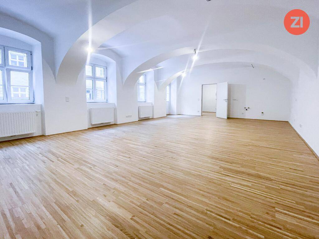 Heller Wohnraum mit mehreren Fenstern, eleganten Gewölbedecken und neuwertigem Holzfußboden.