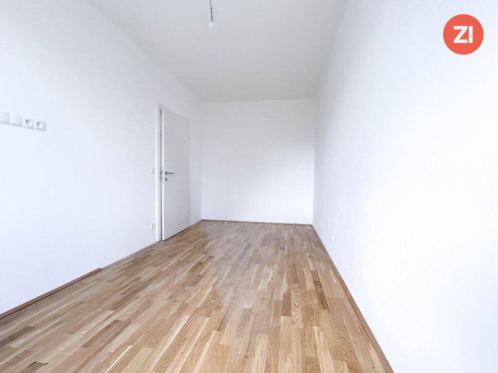 Leeres Schlafzimmer mit hellem Parkettboden und weißen Wänden, bereit für individuelle Gestaltung.