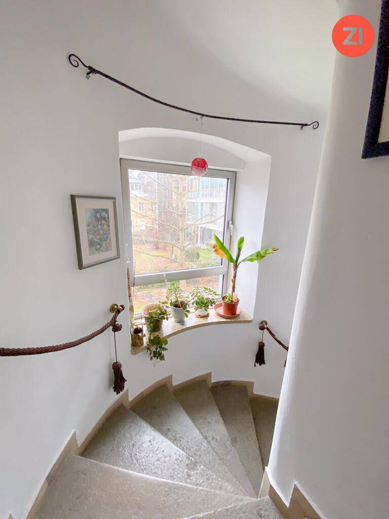 Helle Wendeltreppe mit Steinstufen und einem Fenster, das natürliches Licht in den Flur bringt.