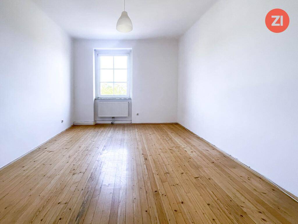 Geräumiges Zimmer mit Holzdielenboden und viel Tageslicht durch das große Fenster.