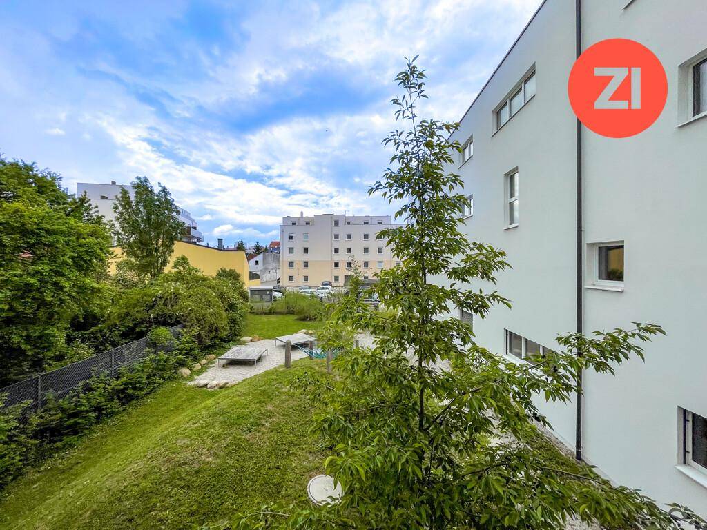 Gemeinschaftlicher Gartenbereich mit Rasenfläche, Bäumen und Spielplatz im Hintergrund.