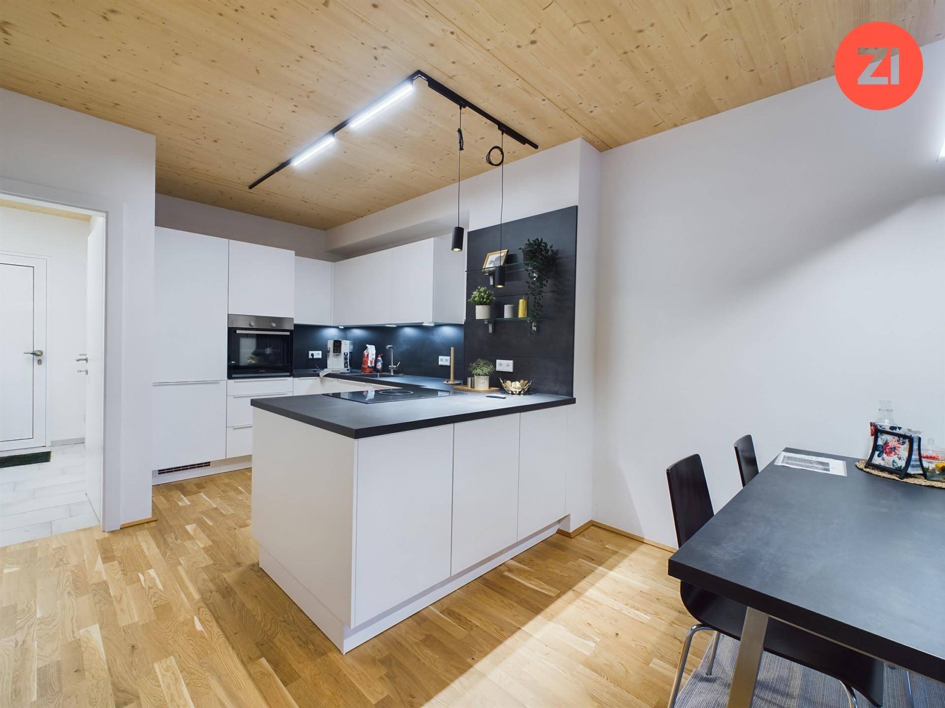 Moderne offene Küche mit weißer Kücheninsel, dunkler Arbeitsplatte und Essbereich mit Holzboden.