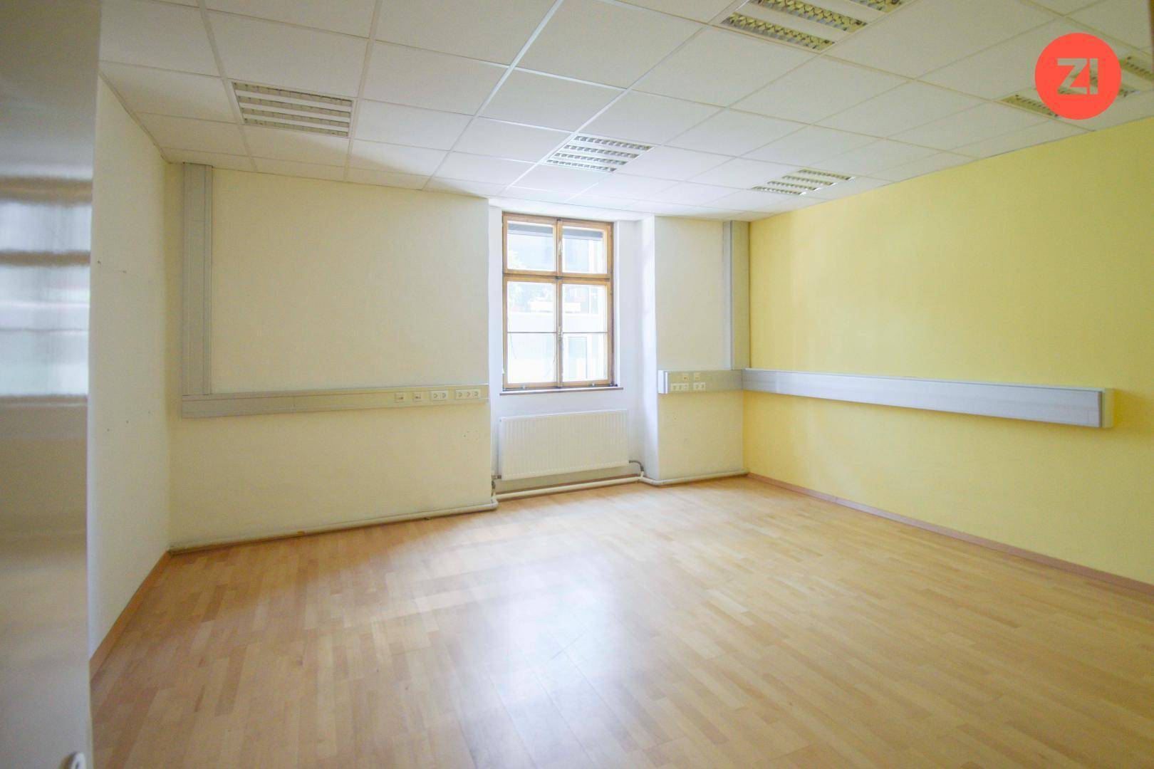 Büro mit gelben Wänden, Fischgrätparkett und großem Fenster, schafft eine freundliche Arbeitsumgebung.