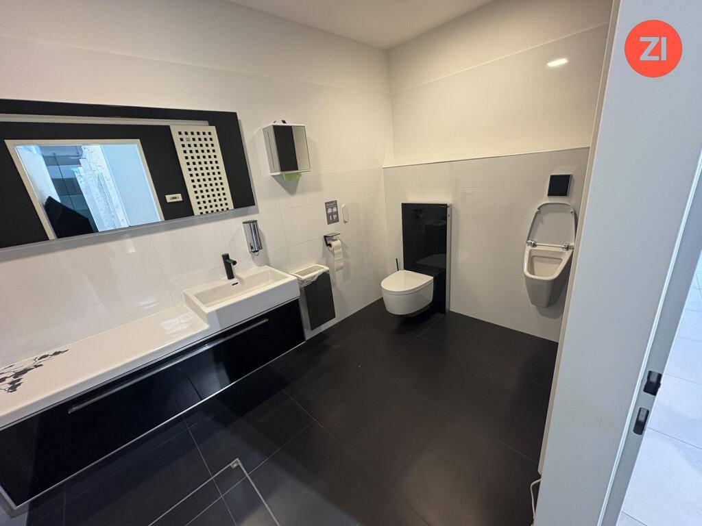 Modernes Badezimmer mit dunklen Fliesen, einem Urinal, wandhängender Toilette und einem breiten Waschtisch.