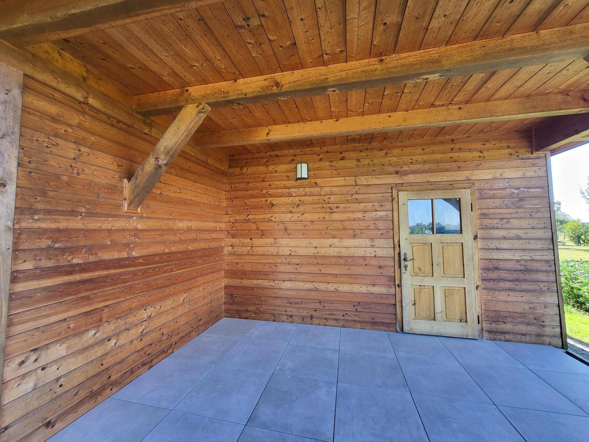 Überdachter Außenbereich mit Holzwänden, Holzdecke und grauen Fliesen, ideal für entspannte Stunden.