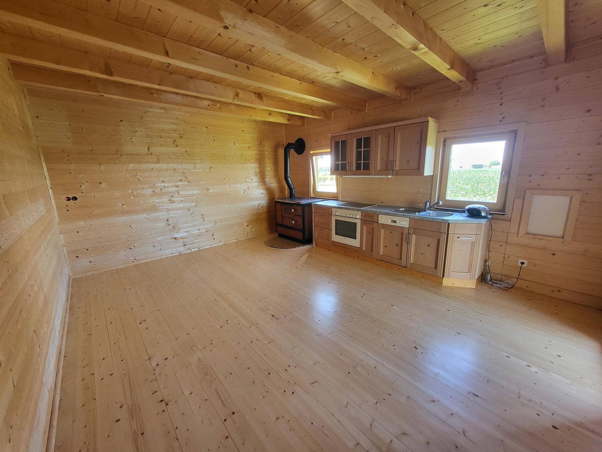 Gemütlicher Innenraum mit Holzwänden und -boden, ausgestattet mit einer Küchenzeile und einem Holzofen.