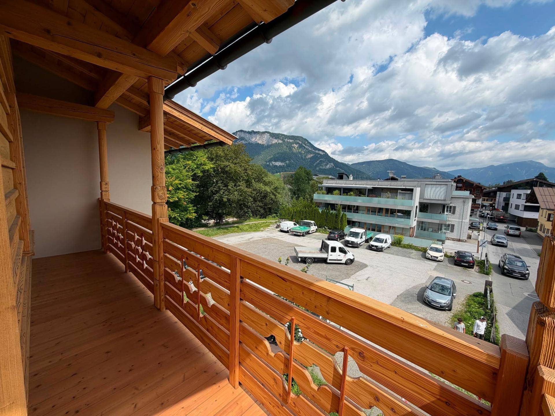 Geräumiger Holzbalkon mit Blick auf einen Parkplatz und die umliegende Berglandschaft.