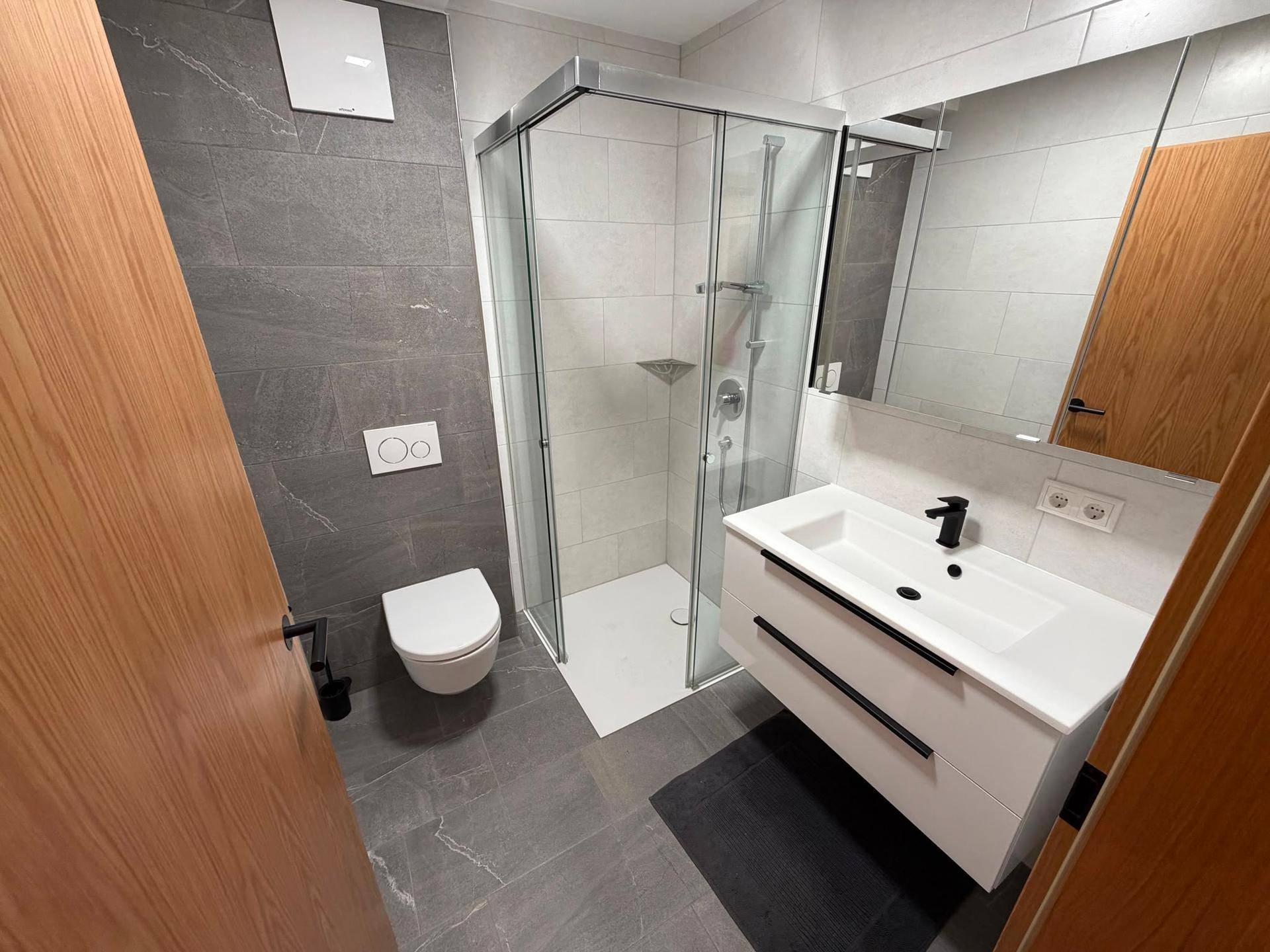 Kompaktes, modernes Badezimmer mit Duschkabine, wandhängendem WC und Einzelwaschbecken.