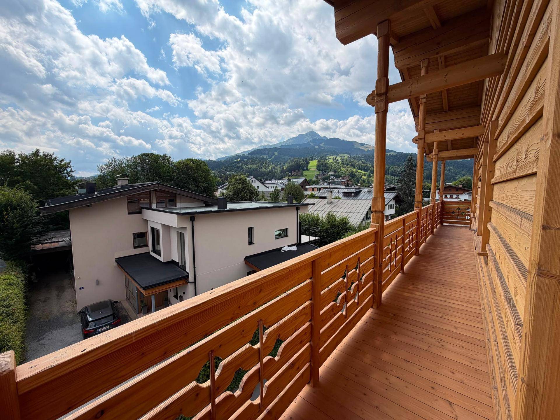Langer Holzbalkon mit traditionellen Schnitzereien und malerischem Bergblick über die Dächer.