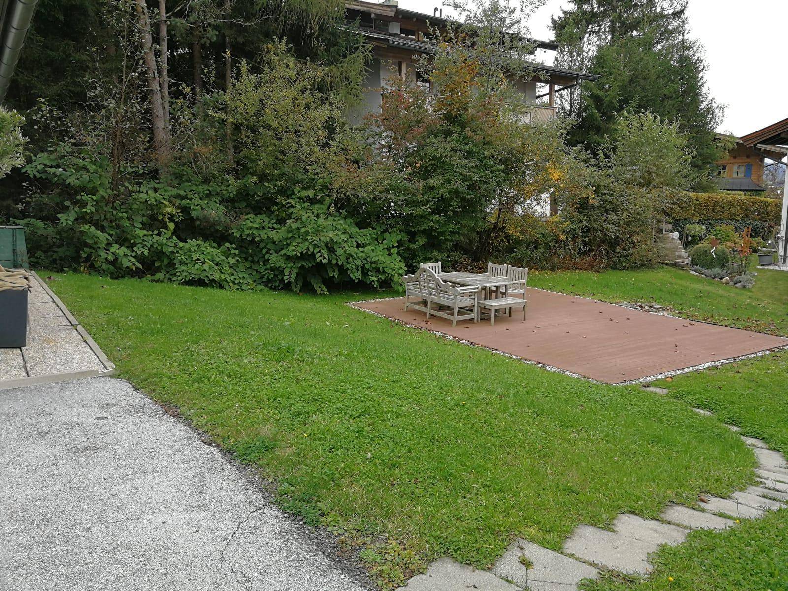 Großer Garten mit Holzterrasse, Gartenmöbeln und viel Grünfläche.
