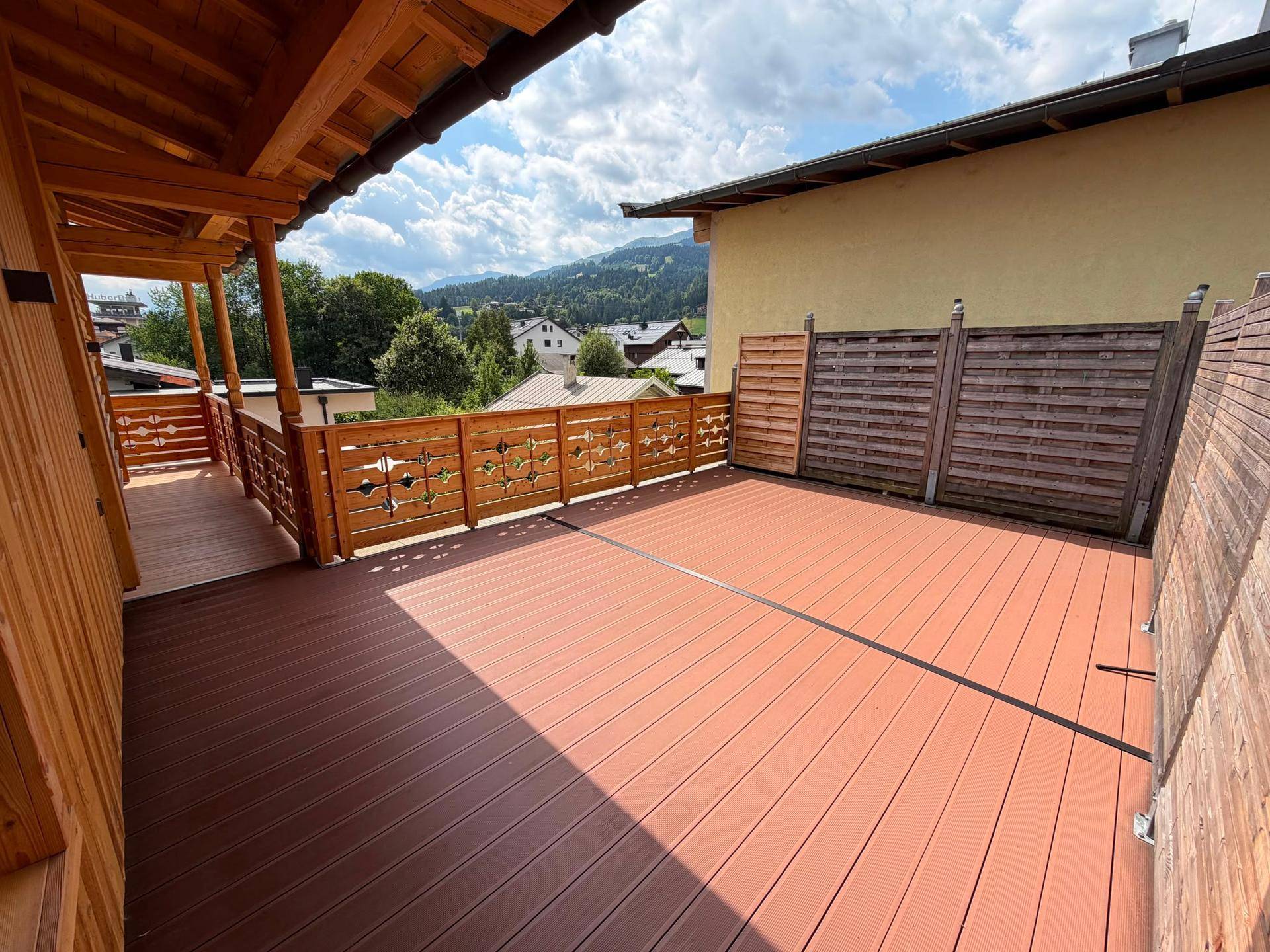 Große Terrasse mit Holzdeck und Sichtschutzwänden, verbunden mit einem traditionellen Holzbalkon.