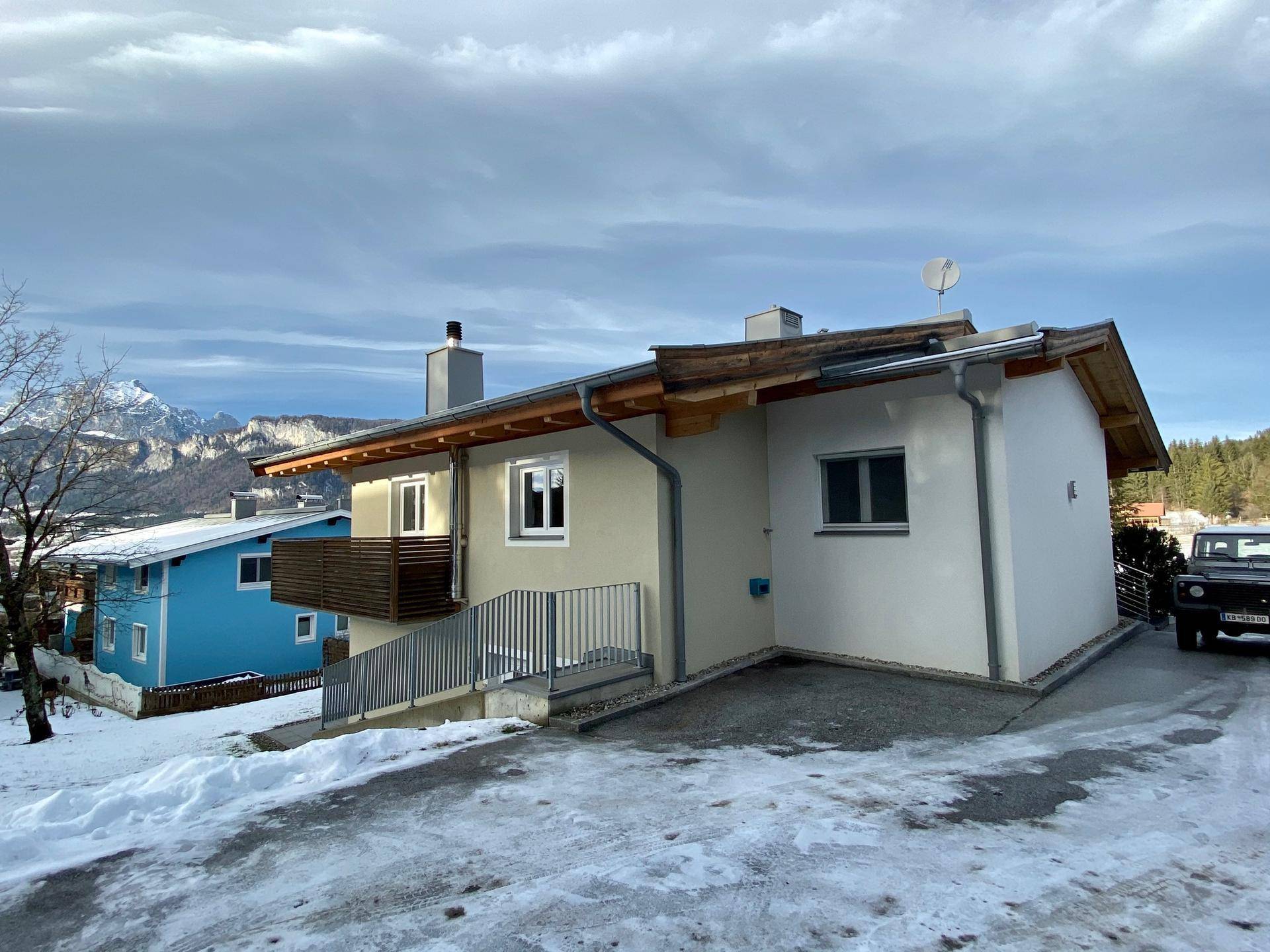 Hausfassade im Winter mit Schnee auf dem Boden und Blick auf die verschneite Umgebung.