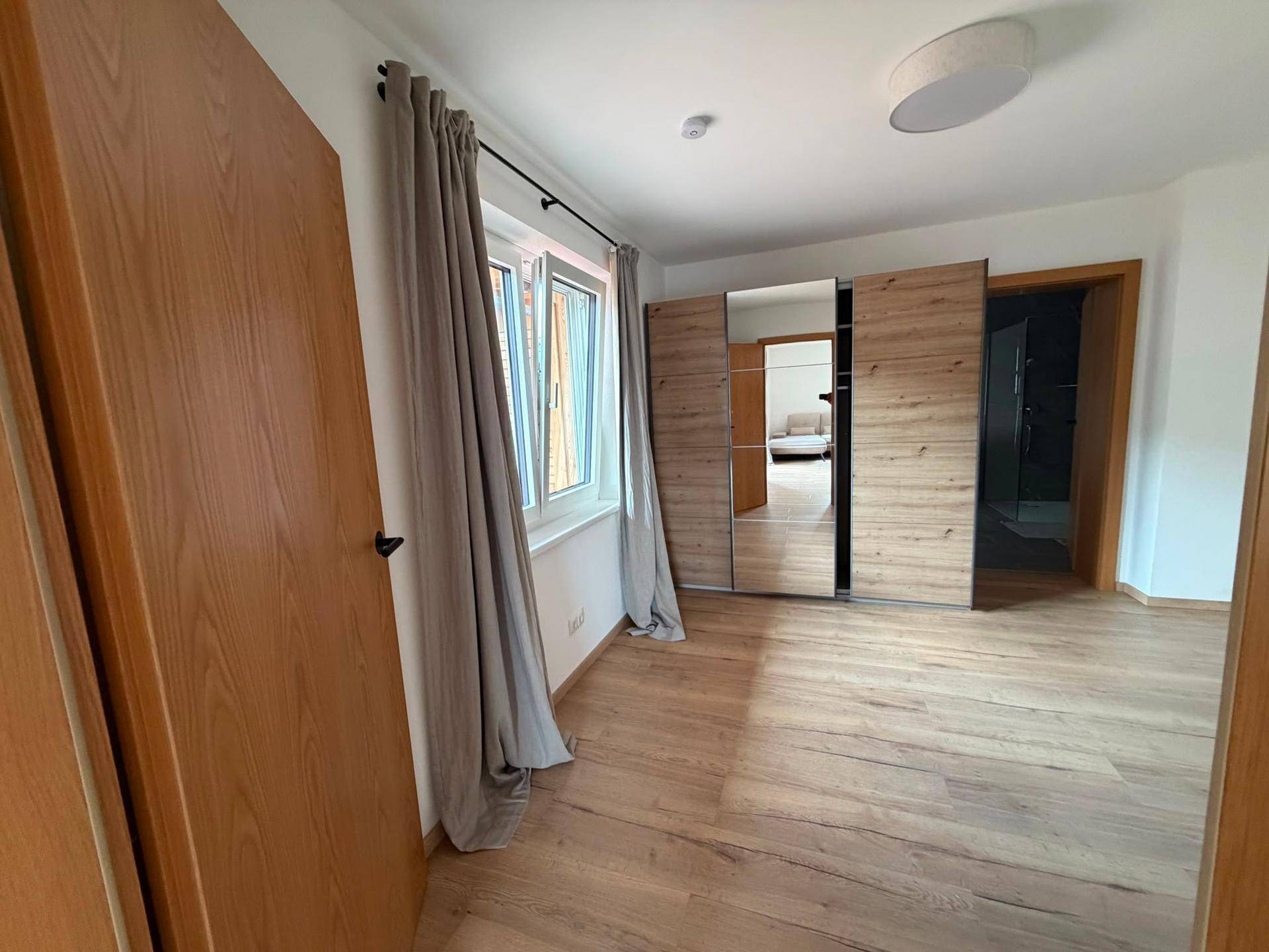 Helles Schlafzimmer mit Holzboden und großem Spiegelschrank, bietet direkten Zugang zum Bad.