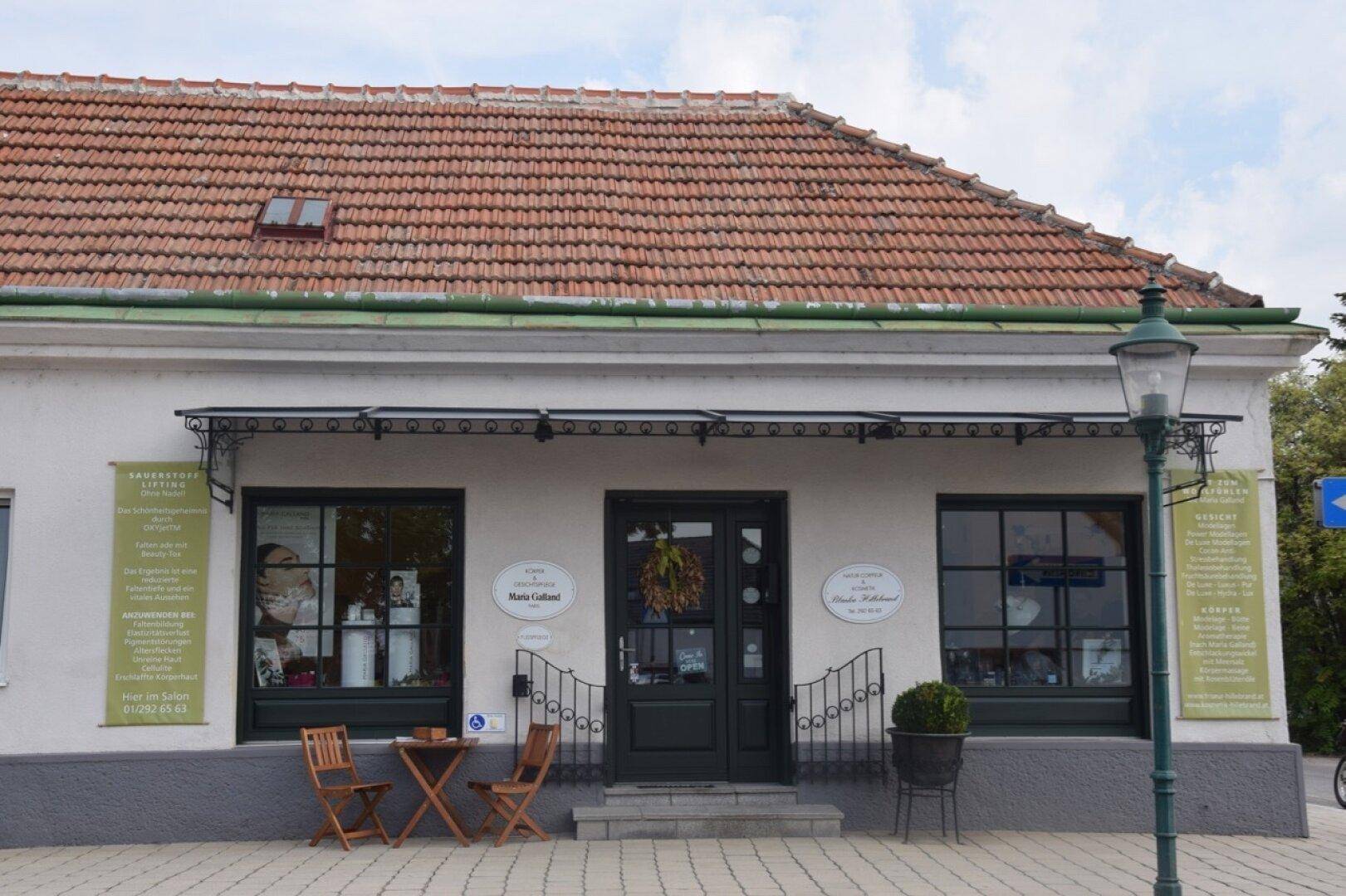 Fassade eines Geschäftsgebäudes mit Ziegeldach, Markise und kleiner Außensitzgelegenheit.