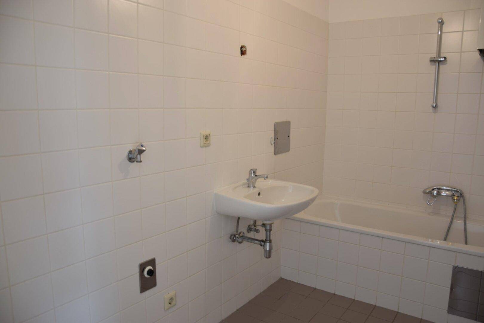 Badezimmer mit Badewanne, Waschbecken und weißen Wandfliesen in gutem Zustand.