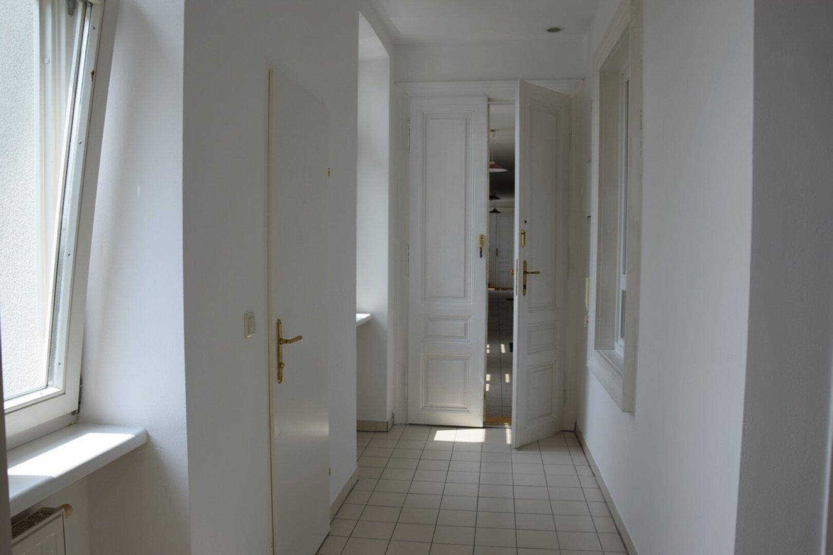 Heller Flur mit Fliesenboden und weißen Türen, der zu weiteren Räumen führt.