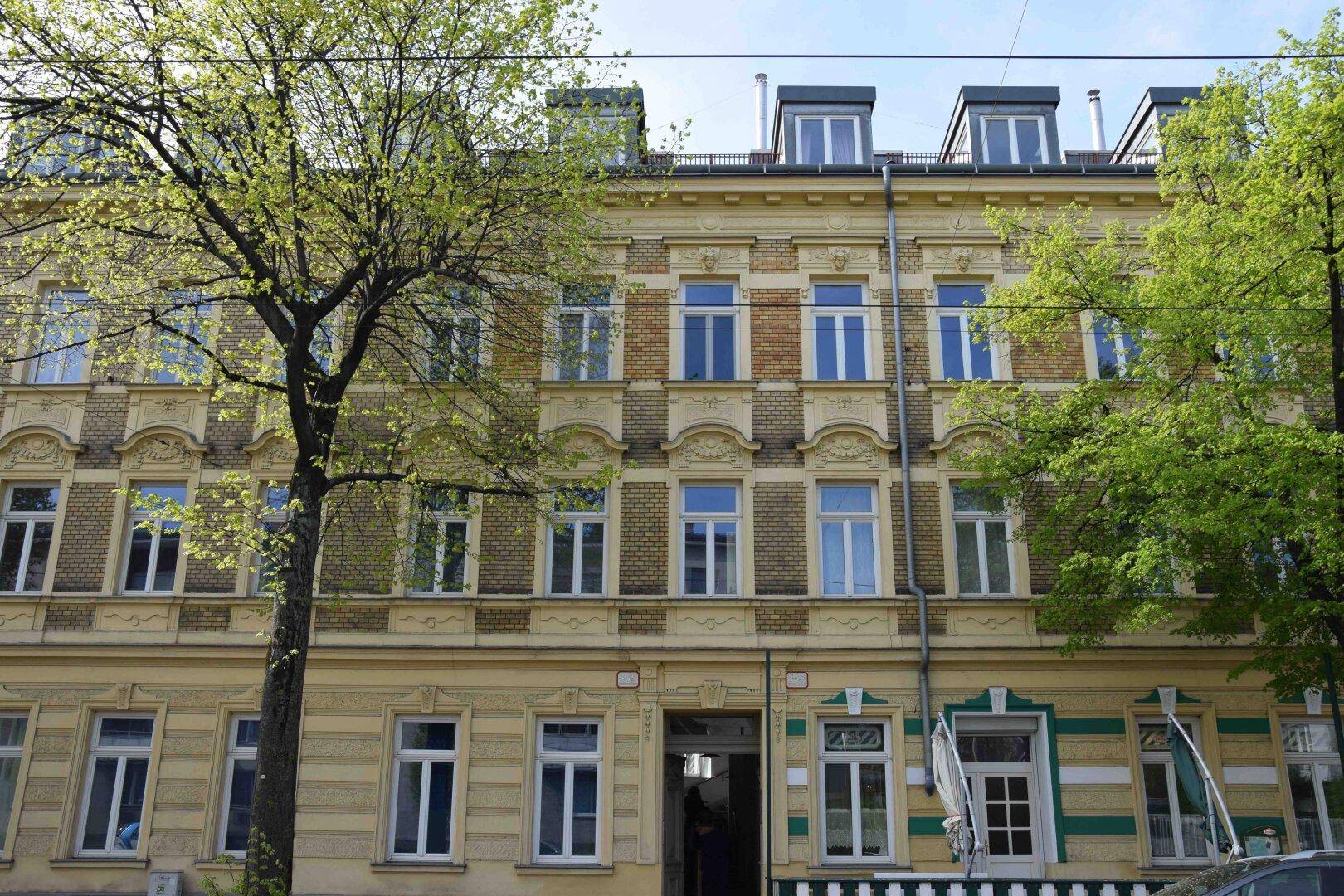 Klassische Fassade eines Mehrfamilienhauses mit vielen Fenstern und Bäumen davor.