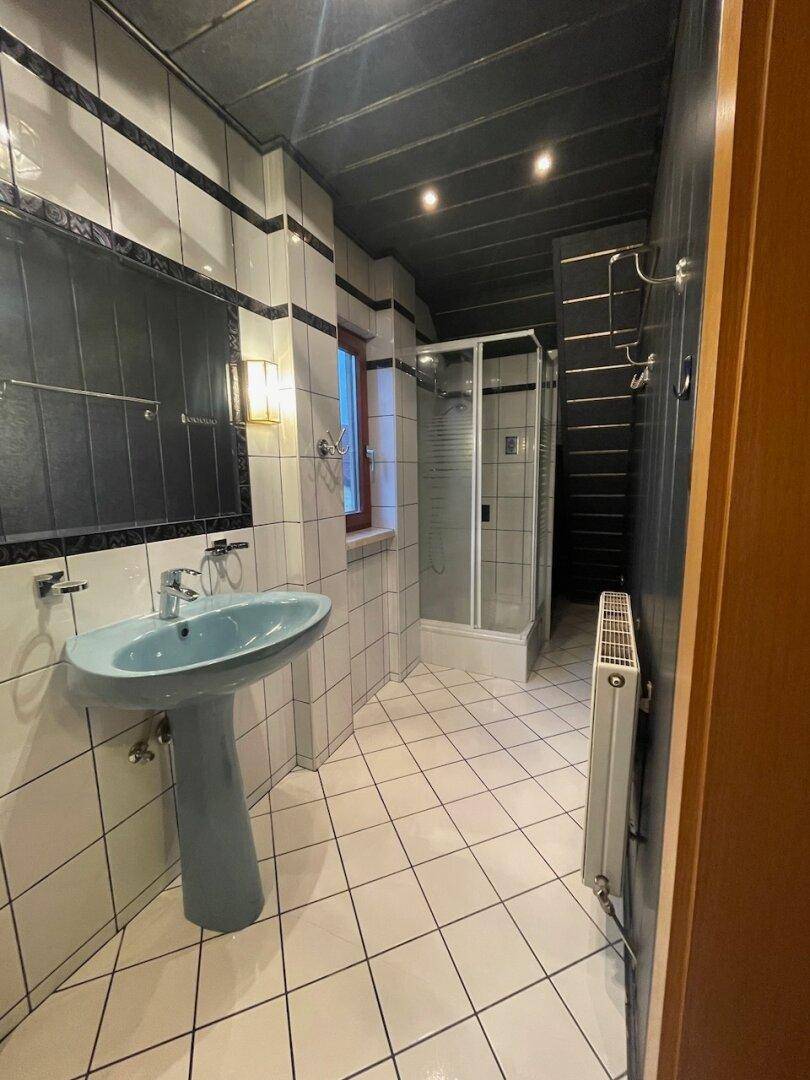 Badezimmer mit weiß-schwarzen Fliesen, blauem Waschbecken und Duschkabine, inklusive Fenster.