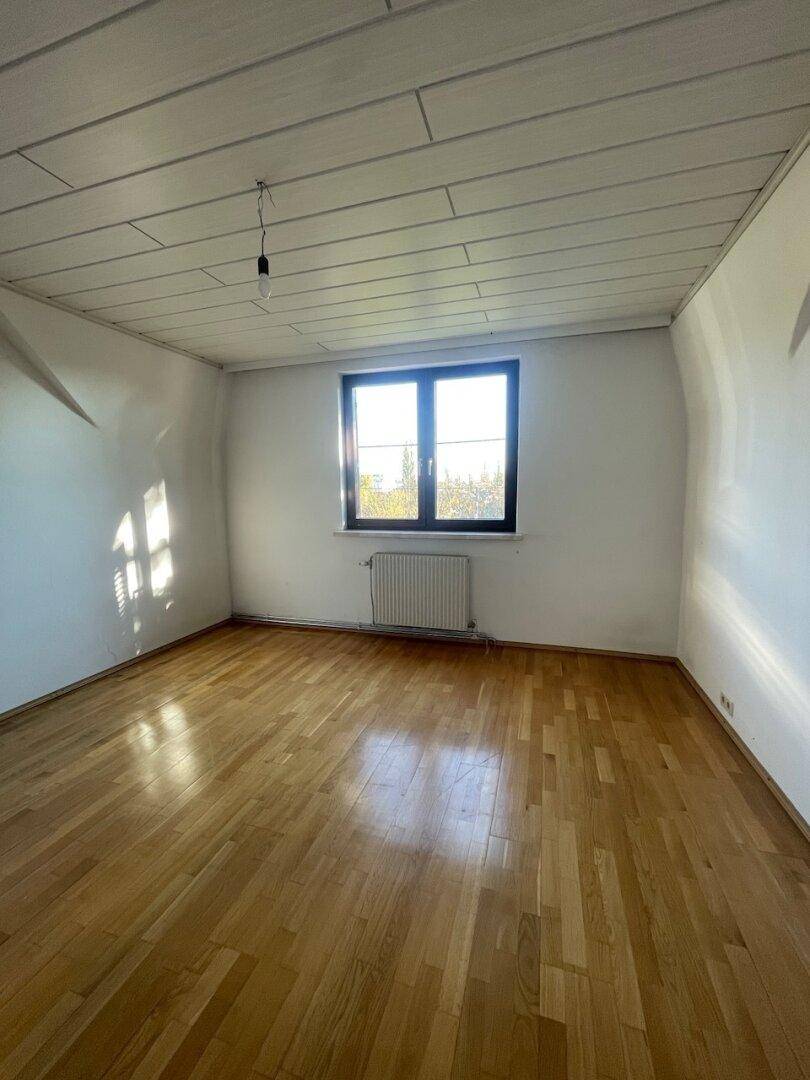 Helles Schlafzimmer mit Holzboden, weißen Wänden und Holzlamellendecke, mit viel Tageslicht.