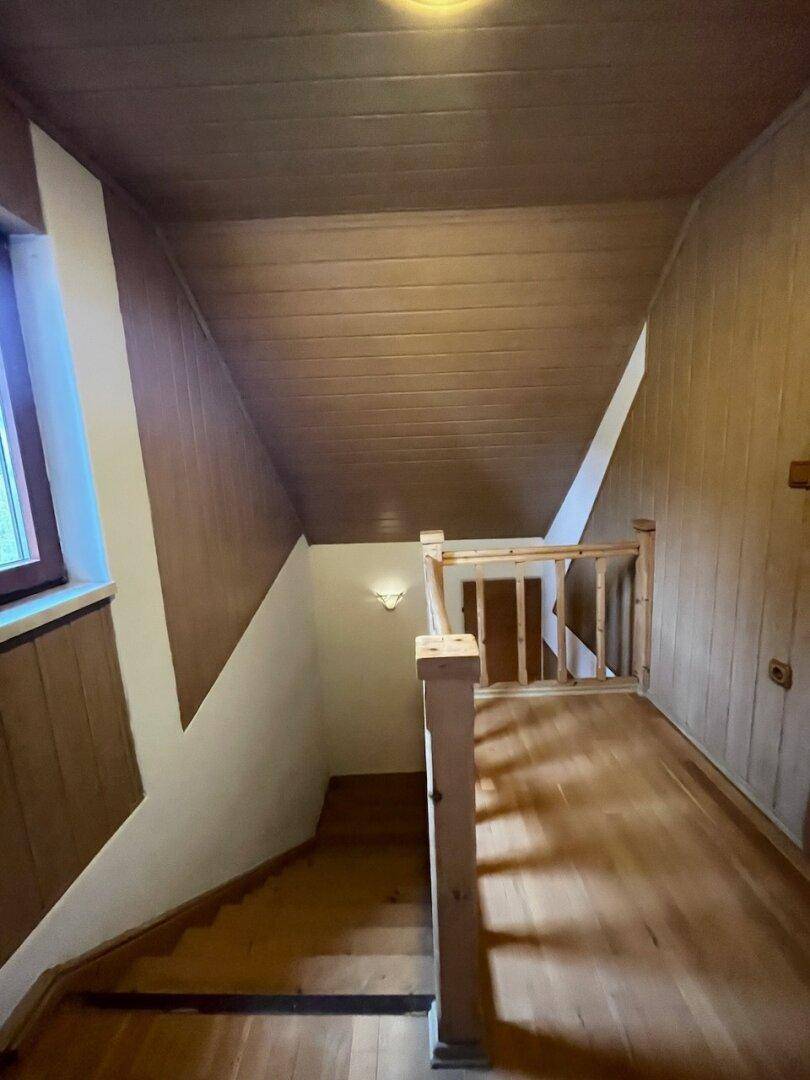Holztreppe mit Holzgeländer und schräger Holzdecke, die in das untere Stockwerk führt.