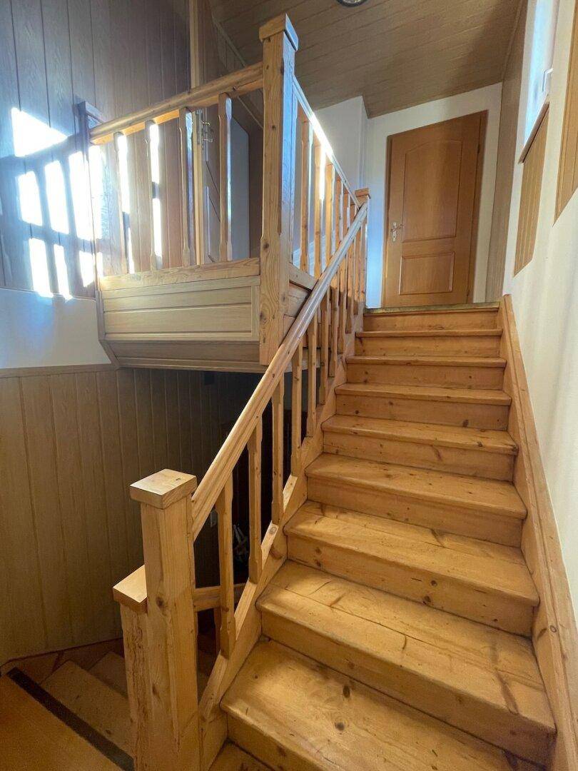 Rustikale Holztreppe mit Geländer und Holzverkleidung, die in die obere Etage führt.