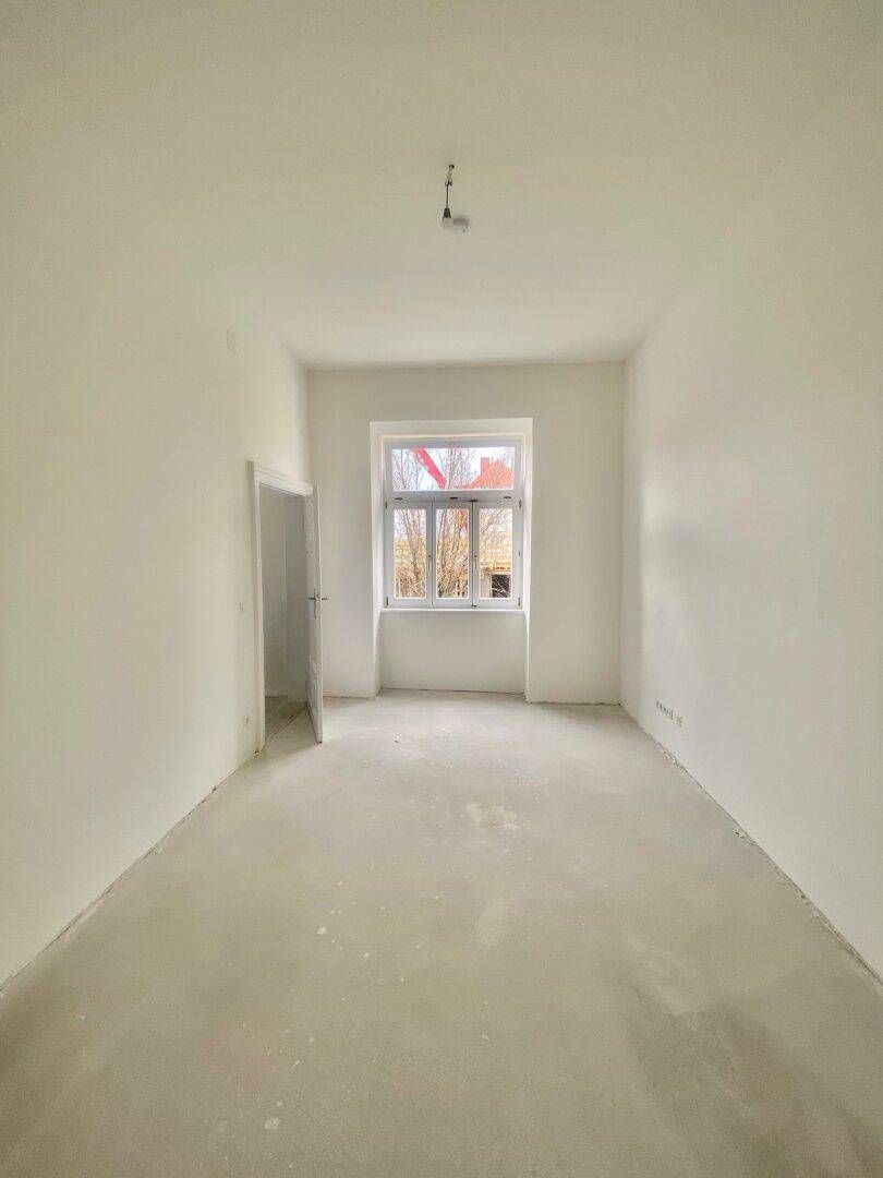 Leerer Raum mit einem großen Fenster, das viel Tageslicht hereinlässt, ideal für Schlafzimmer oder Büro.