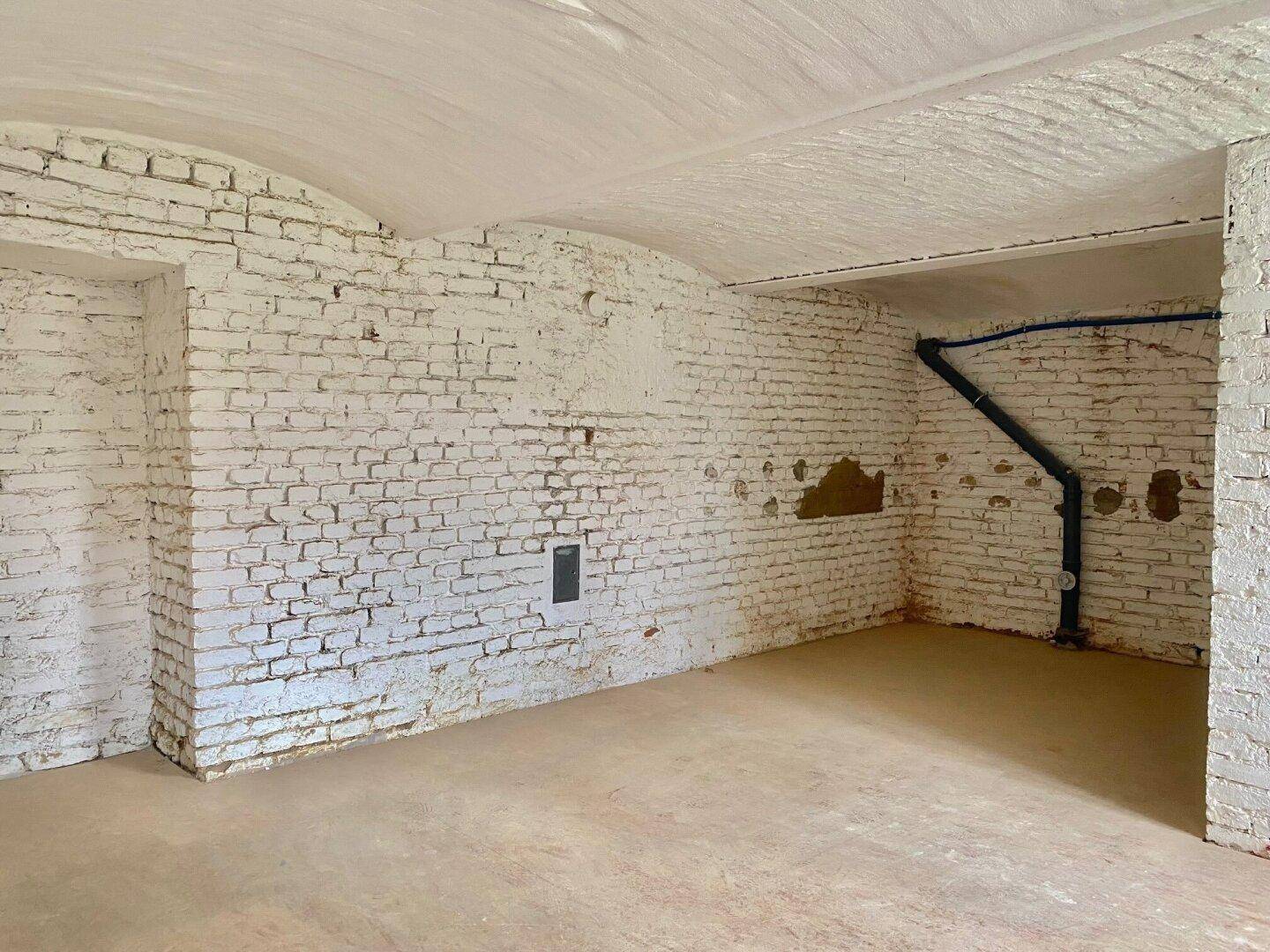 Geräumiger Kellerraum mit weiß getünchten Ziegelwänden und sichtbaren Rohren an der Decke.