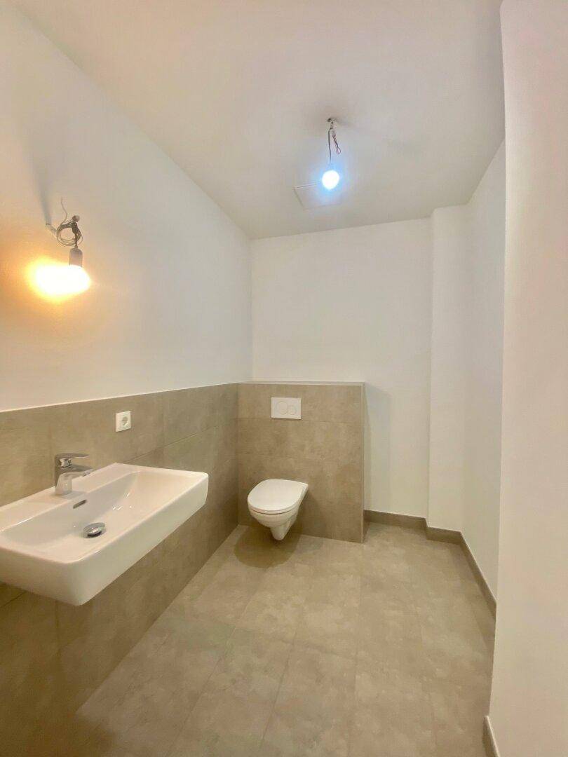 Modernes Badezimmer mit Wand-WC und Waschbecken, halbhoch gefliest in neutralen Farbtönen.