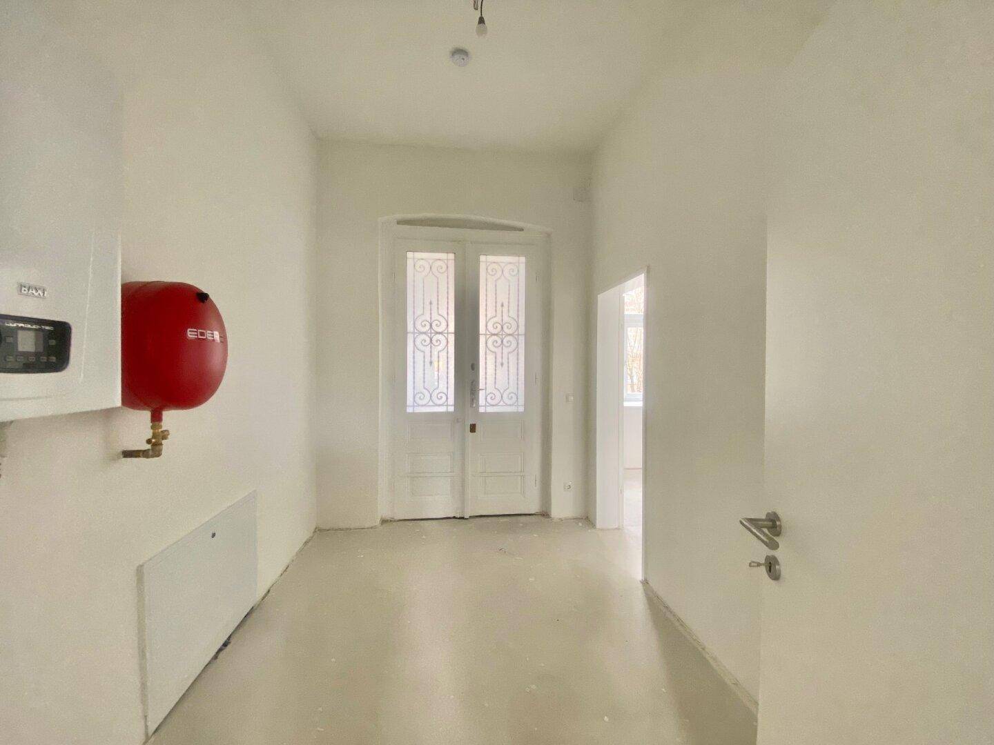 Heller Eingangsbereich mit weiß gestrichenen Wänden und einem Warmwasserbereiter an der Wand.